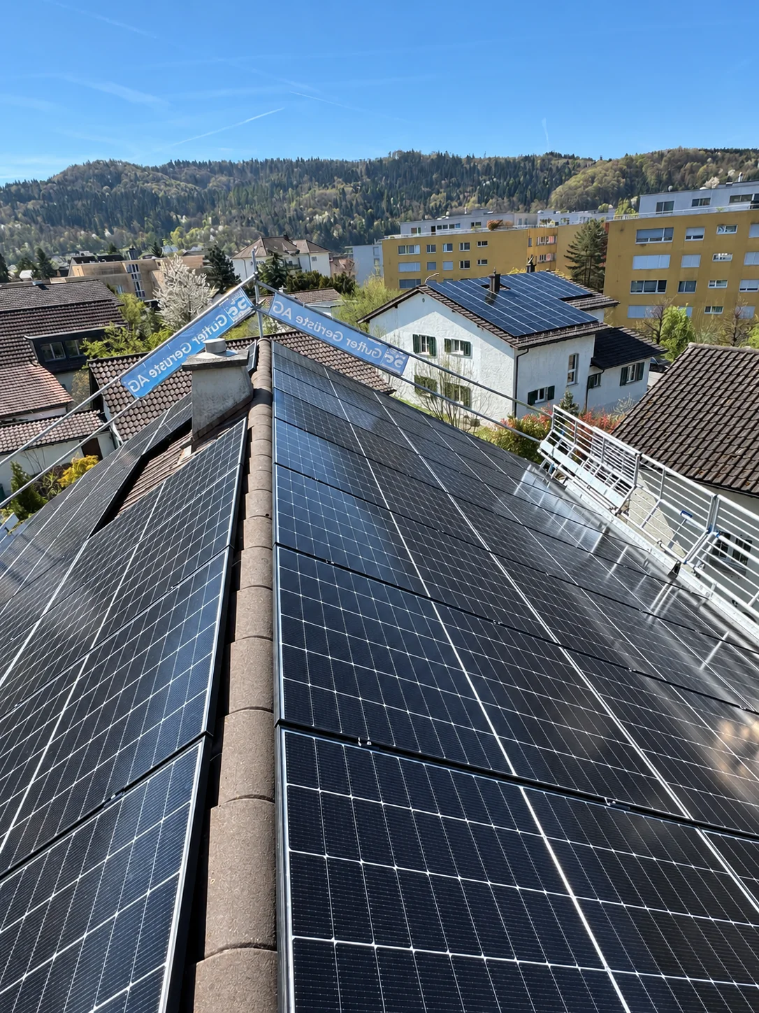 Blick über den Dachfirst mit Solarmodulen auf beiden Dachseiten in Richtung Wohnquartier
